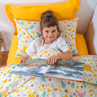 Enfant lisant dans un lit avec du linge de lit motif forêt, ambiance cocooning.