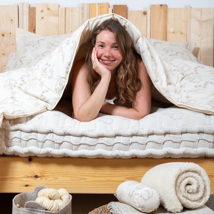 Femme allongée sur le ventre, souriante sous une couette en laine, sur un matelas naturel.