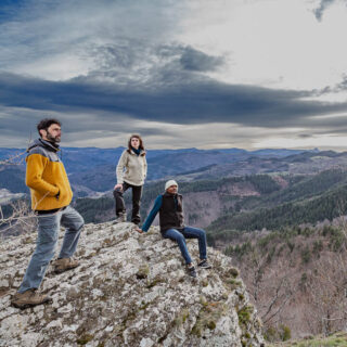 Deux hommes et une femme portant des vêtements chauds posent sur un rocher avec vue sur l’Ardèche en hiver.