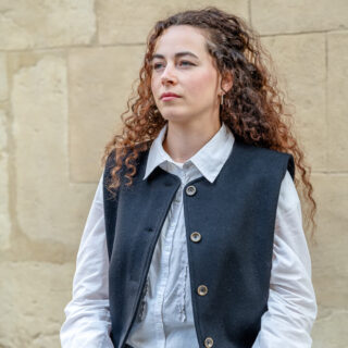 Femme élégante portant un veston en feutre de laine devant un mur beige en ville.