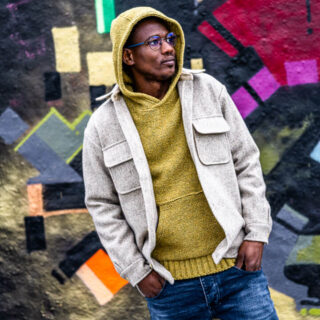 Homme portant un pull à capuche et une chemise en laine devant un mur de graffitis.