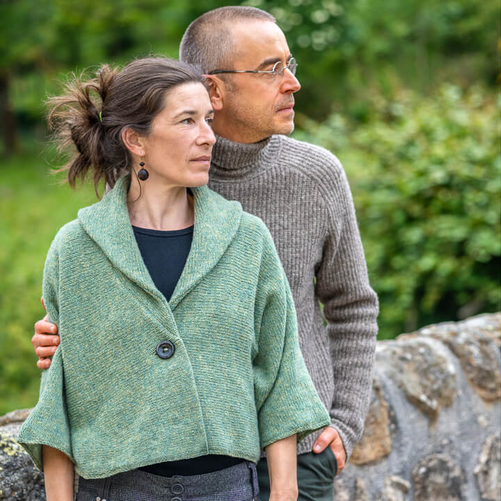 Couple portant un pull et un gilet en laine sur un pont en pleine nature verdoyante.