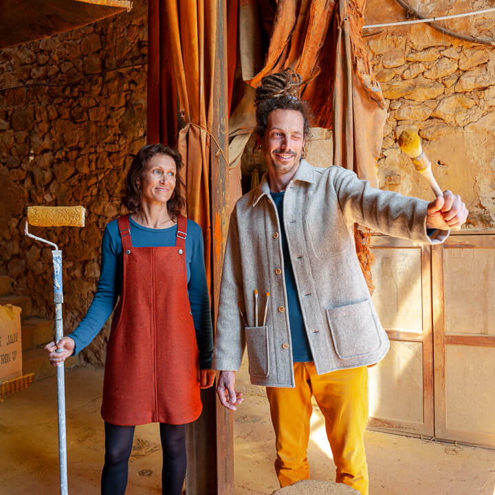 Homme et femme portant des vêtements en laine recyclée dans un atelier d’artiste, pinceaux à la main.