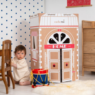 Jeune enfant jouant à côté d'une cabane en carton illustrée représentant une maison classique.