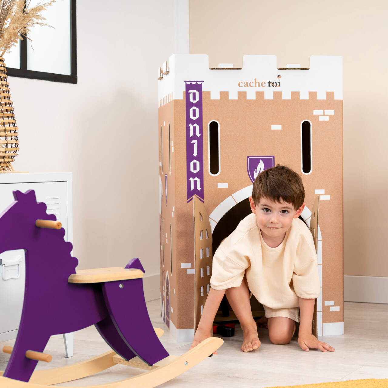 Petit garçon souriant à l'intérieur d'une cabane en carton en forme de donjon médiéval.